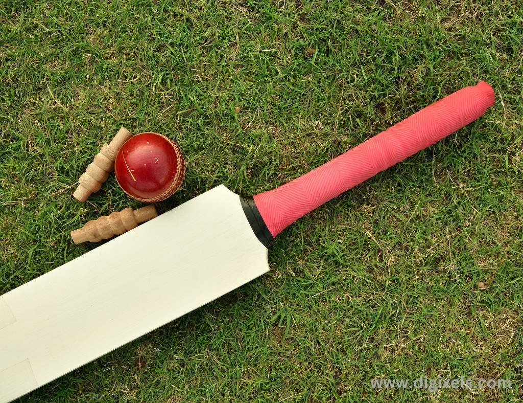 Cricket images of cricket bat, red ball and bell kept on the ground.